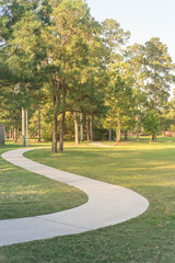 Concrete winding concrete pathway and tall trees at green suburban park in Houston, Texas, USA