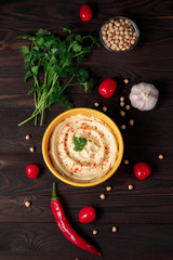 Plate of spicy traditional hummus with pepper and greens on a wooden background. Colorful hummus bowls decorated with chickpeas, herbs, garlic, tomate and chili pepper. Top view