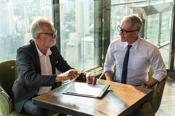 Picture of two business man discussing business on a table.  The young man is wearing a white shire...