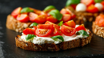 Bruschetta with ricotta cheese, basil, cherry tomato on rustic stone board