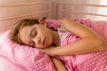 Obraz na płótnie Canvas Little sick child is sleeping in bed with fever. She sleeps in a tubular bed covered with pink blanket in pink sheets and pillow.