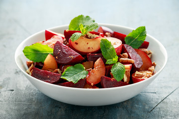 Vegan Plum, beet salad with pecan nuts, mint and herbs in white bowl. healthy summer food.