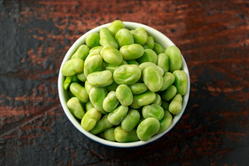 Green Broad Beans in a blue bowl on wooden table. healthy food