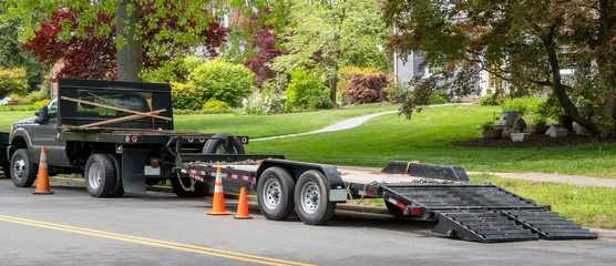 Landscaping truck with empty flatbed trailer with ramp parked on residential neighborhood street.