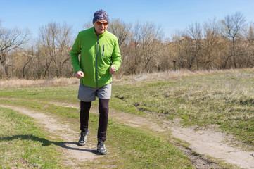 Caucasian senior man running lonely on a country road at early spring season