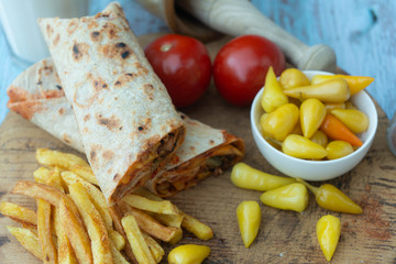 Doner kebab (shawarma or doner wrap). Grilled chicken on lavash (pita bread) with tomatoes, green salad and peppers on the old wooden background. Middle Eastern food, arabic fast food concept