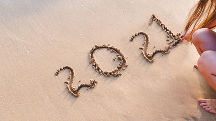 woman writting 2021 on sand beach. ocean wave and lettering on the beach. Happy New Year 2021. tropical vacation 2021.