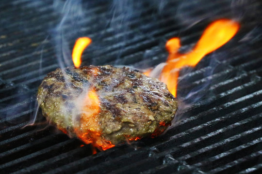 Burger Barbeque Being Cooked On Hot Grill With Smokey Fire.