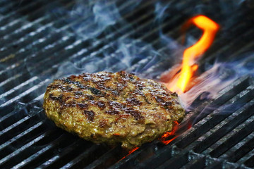 Burger barbeque being cooked on hot grill with smokey fire.