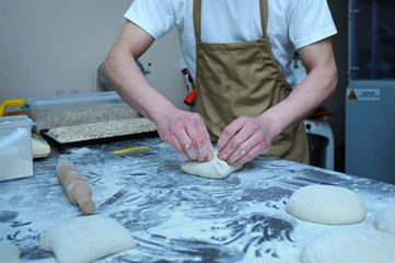 At the bakery: baker standing at a work table and forming dough for baking bread