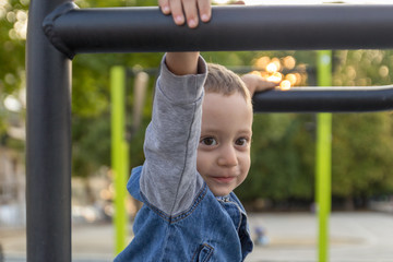 Obraz premium Happy small boy hanging on brachiating bar at a school yard. Selective focus.