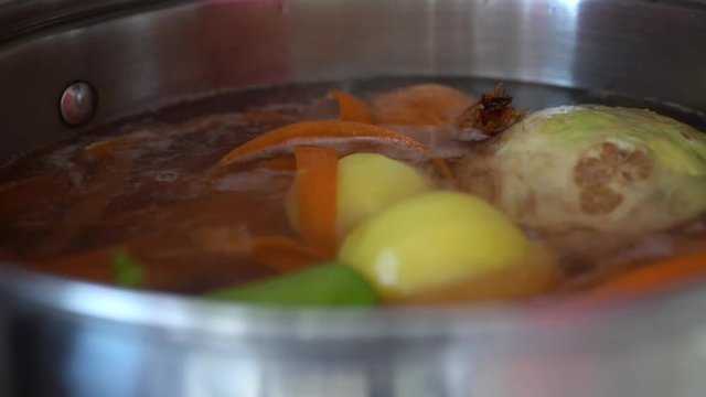 Close up view of potatoes falling into pot filled with variety of root vegetables for stock.
