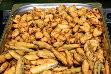 Large group of freshly fried mussels and small fishes on display for sale at a street food festival, ready to eat healthy seafood, beautiful orange monochrome outdoor background
