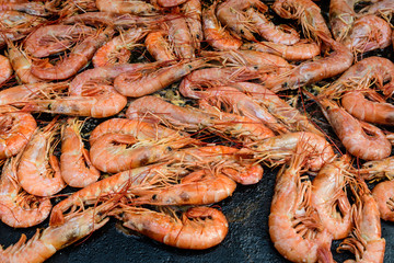Close up of large portion of grilled shrimps on a large black pan at a street food festival, ready to eat healthy seafood, beautiful orange monochrome outdoor background
