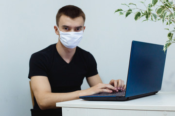 Man with mask and laptop working from home while corona virus illness do not stop. Home working concept.