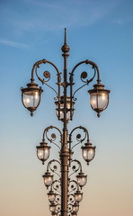 Openwork wrought iron street lamps against the sky.
