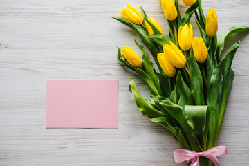 Craft pink postcard with bouquet of yellow tulips on wooden background. Space for message. Spring flowers. Holiday greeting card for Valentine's, Women's, Mother's Day, Easter! Top view, flat lay. © Serhii