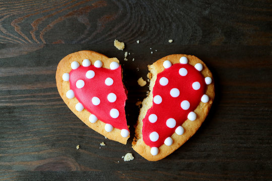Broken red and white heart shaped royal icing cookie on dark color background