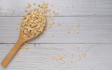 Rolled oats or oat flakes in Wooden spoon on white wood background. Top view, horizontal. Healthy lifestyle, healthy eating, vegan food concept