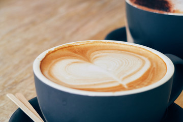 A beautiful creamy brown warm fresh cappuccino coffee cup, full of creamy coffee, served in a wooden rustic brown coffee shop with coffee art. Organic fair trade coffee photographed from the side