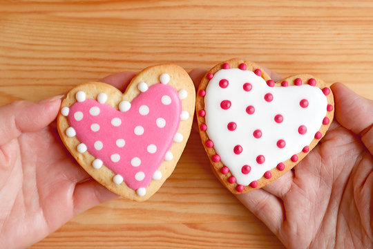 Pink and white dotted heart shaped cookies in couple's hands put together on wooden background