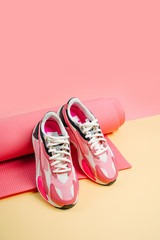 Pair of bright women's sneakers with pink yoga mat on yellow  background. Healthy lifestyle...