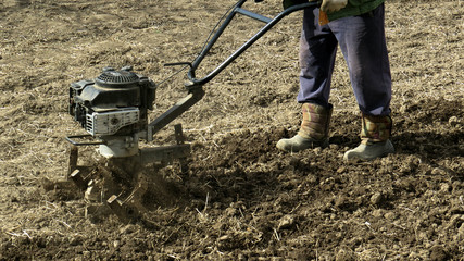 Legs of a man in a boot with a cultivator. Tillage. Spring work in the garden. Gardening concept
