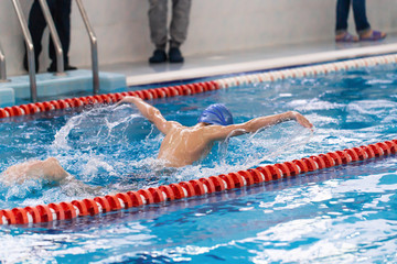 Swimming pool athlete training indoors for professional competition. Teenager swimmer performing the butterfly stroke at indoor swimming competition