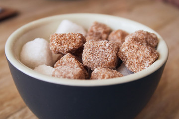 A bowl of brown crystallised sugar cubes in a hipster coffee shop on a rustic brown table, photographed with a shallow depth of field. Sugar cubes perfect for tea and coffee hot drinks.
