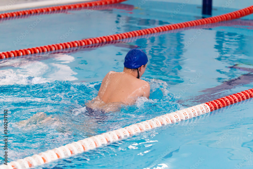 Wall mural Swimming pool athlete training indoors for professional competition. teen swimmer performing the breaststroke at indoor swimming competition