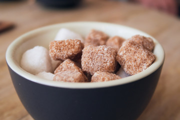 A bowl of brown crystallised sugar cubes in a hipster coffee shop on a rustic brown table, photographed with a shallow depth of field. Sugar cubes perfect for tea and coffee hot drinks.