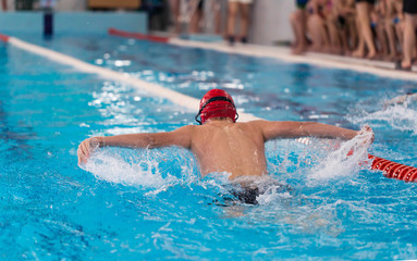 Swimming pool athlete training indoors for professional competition. Teenager swimmer wearing red...