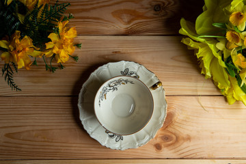 Kompozycja filiżanki na tle sosnowych desek oraz kwiaty. © Mariusz