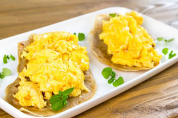 Scrambled eggs on top of pita bread with young leaves of green basil on white plate.