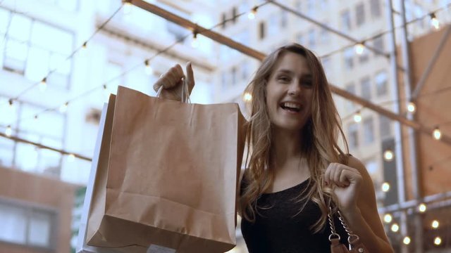 Portrait of young happy beautiful woman standing in the shopping center and showing the bags from shops with purchases.