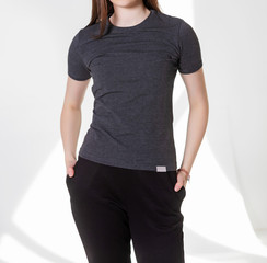 Young girl wearing blank t-shirt and and sport pants. Gray wall background shadow light from the window with copy space for your text message or promotional content