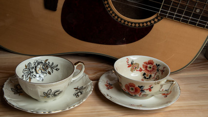 Kompozycja filiżanek i gitary na tle sosnowego stołu. © Mariusz