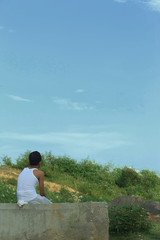 Fototapeta na wymiar a teenager boy sitting roadside wearing traditional bengal dress dhoti and looking at the nature and blue sky