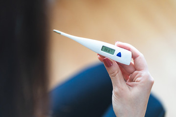 Selective focus of a woman holding a digital thermometer that indicates she has over 38 degrees fever. Sick and worried female with fever and illness during pandemic. 