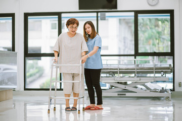 young physical therapist helping senior patient in using walker during rehabilitation