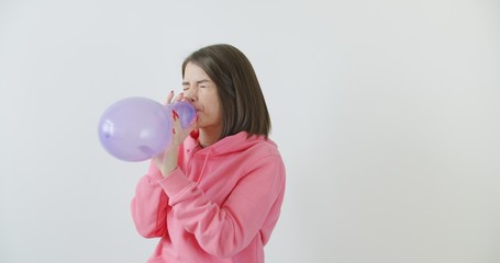 Young woman blowing a pink balloon