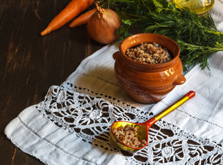 Buckwheat porridge in a pot and a wooden painted spoon on a linen napkin, vegetables in the...