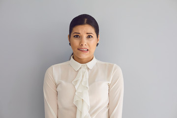 Tense young woman looking at camera on gray wall