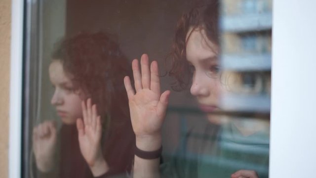 Two sad curly children, brother and sister, a boy and a girl behind a glass near the window. Quarantine Coronovirus Covid-19