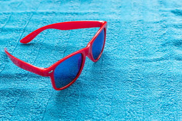 Fashionable red sunglasses with blue glasses on blue beach towel. Travel and summer vacation concept.
