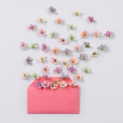 Creative layout made with open paper envelope and many vibrant little florets on pastel white background. Spring awakening concept.