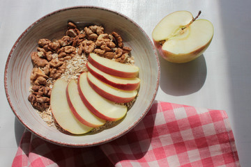 Healthy Walnut Red Apple Oatmeal in the vintage bowl on a red and white checkered cloth napkin. Natural lighting. Beautiful openwork shadow from the curtain. Top view.