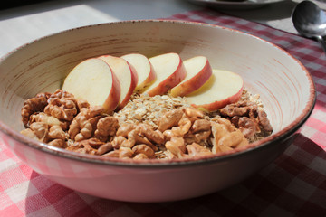 Healthy Walnut Red Apple Oatmeal in the vintage bowl on a red and white checkered cloth napkin. Natural lighting. Beautiful openwork shadow from the curtain. Top view.