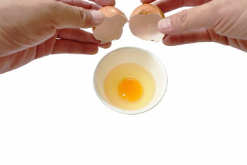 hand opened shell and raw egg with yolk dropping in cup on white background