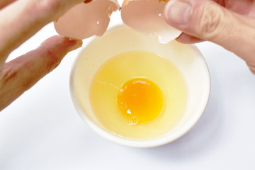 hand opened shell and raw egg with yolk dropping in cup on white background